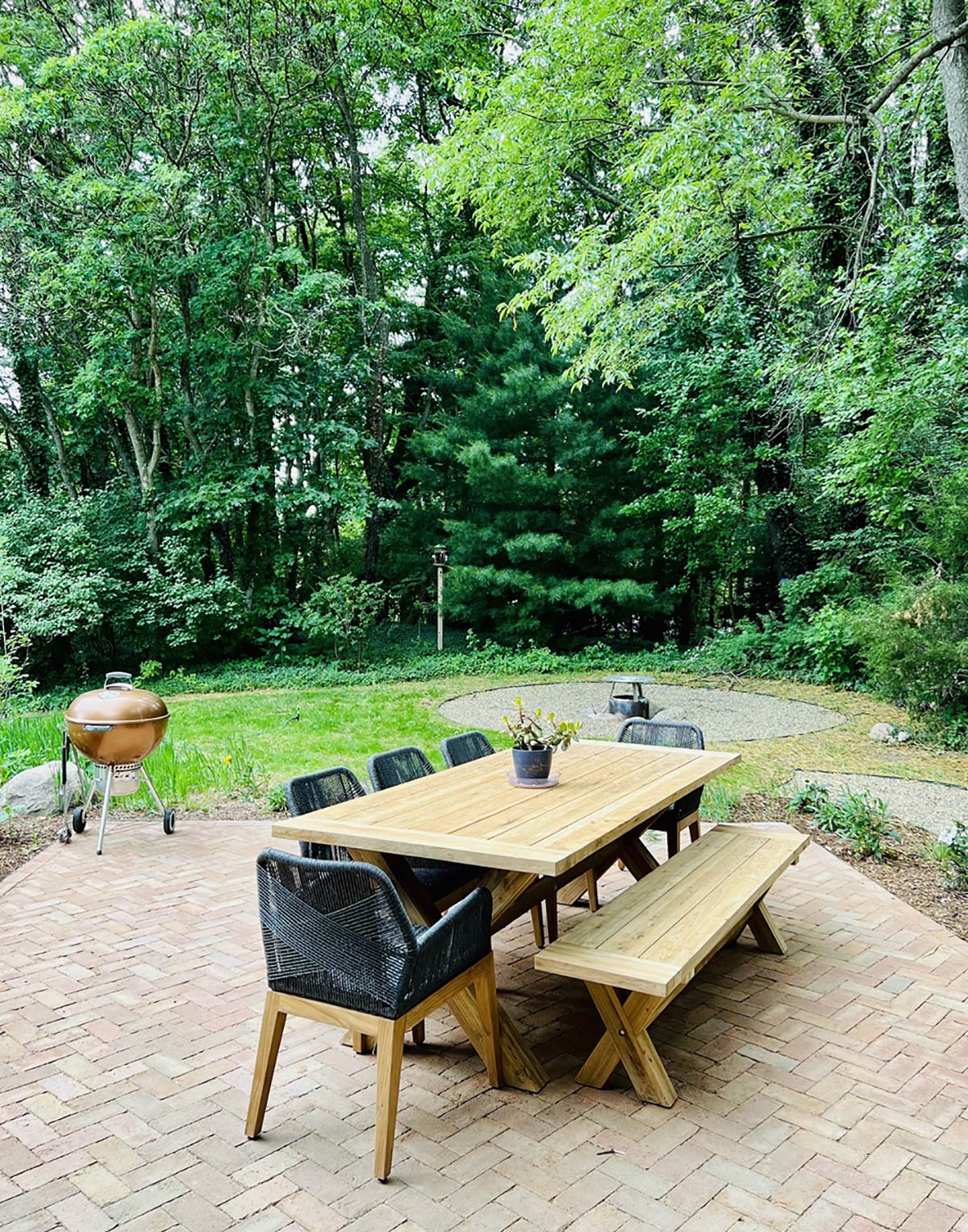large table chairs and bench on patio surrounded by trees