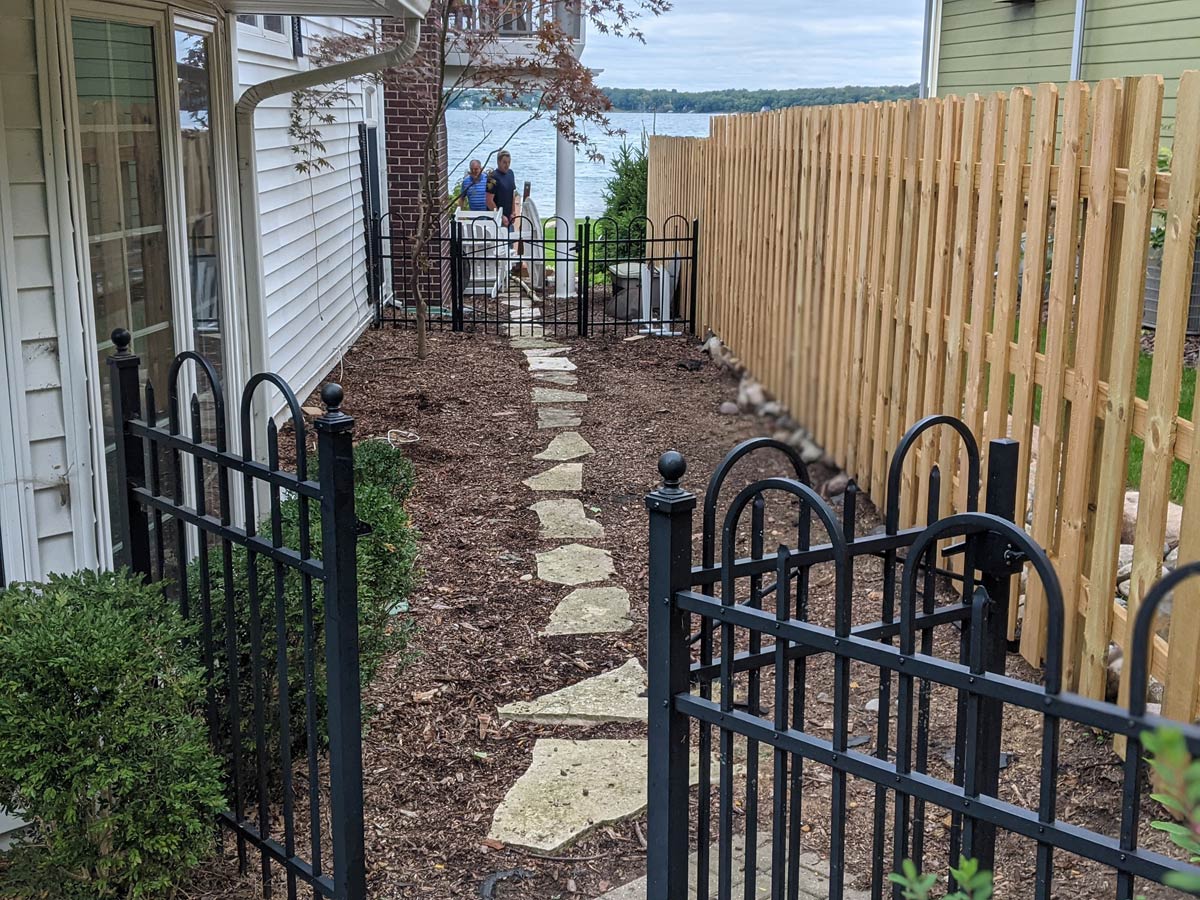 metal gate leading to stone path along wooden fence